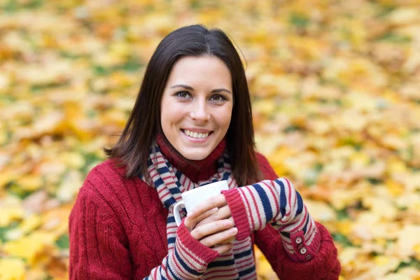 Young smiling woman with cup of tea in an autumn park