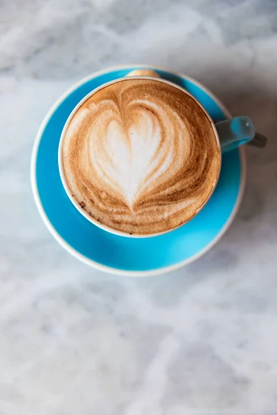 Fresh coffee with heart love foam in blue cup on marble background