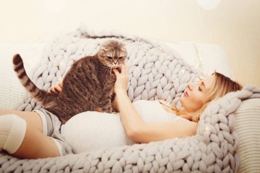 Happy pregnant woman relax with cat on a sofa clipart