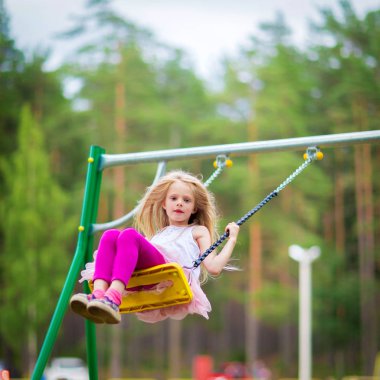 Küçük sarışın kız açık havada sallanan bir playgroung çocuklar için gülümseyen