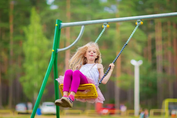 Küçük sarışın kız açık havada sallanan bir playgroung çocuklar için gülümseyen