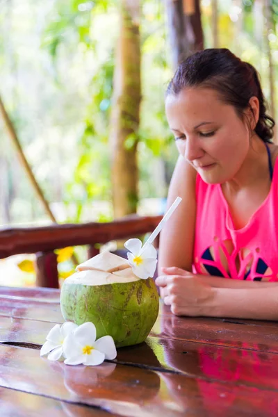 Tropikal palmiye yaprakları ve beyaz frangipani çiçeklerle kadının tropikal bar önünde taze Hindistan cevizi keser