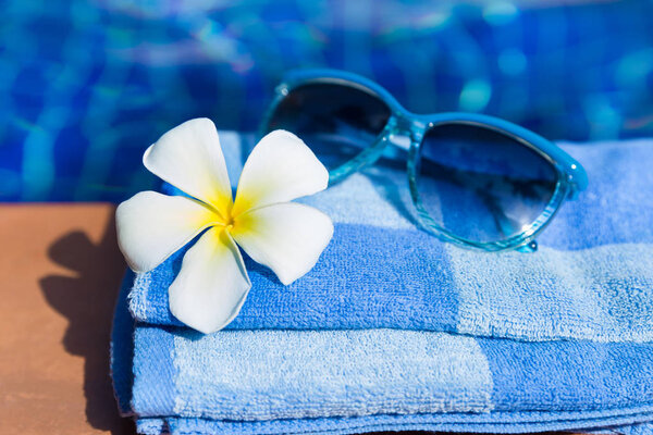 Fluffy towel with sunglasses and flower on border of a swimming pool