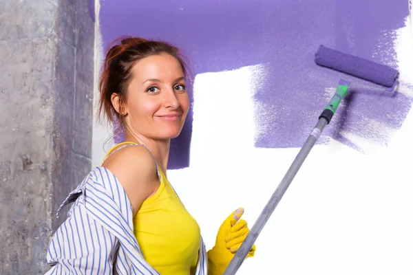 Ung attraktiv kvinna målar vit vägg med lila färg roller — Stockfoto