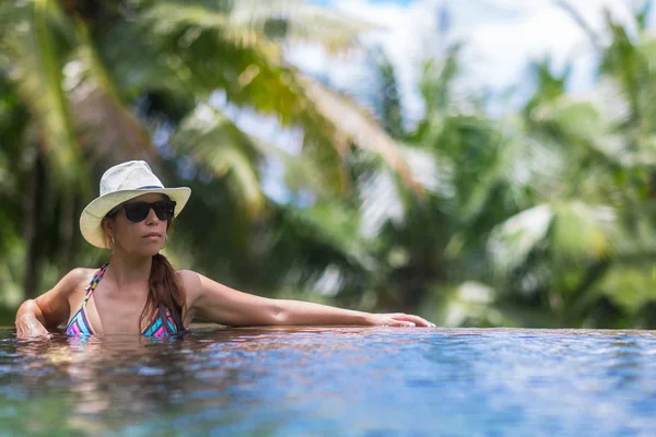 Junge schlanke brünette Frau sonnt sich im tropischen Pool — Stockfoto