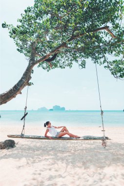 Beyaz deniz sahilinde salıncakta sallanan genç bir kadın