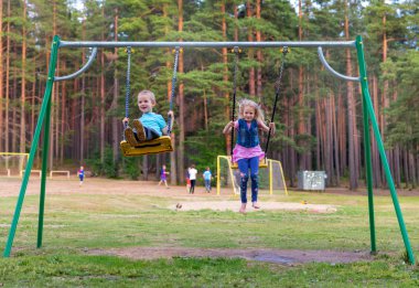 Pretty küçük sarışın kız ve erkek oyun alanında açık havada sallanan