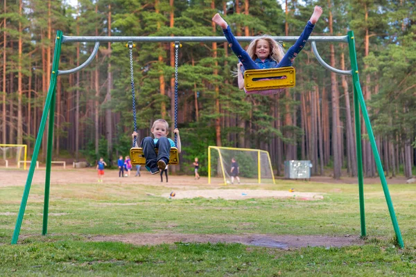 Linda menina loira e menino balançando ao ar livre no playground — Fotografia de Stock