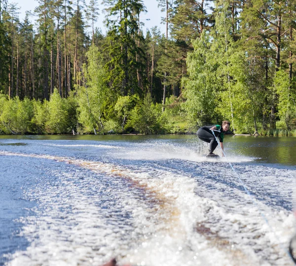 Young pretty slim brunette woman in wetsuit riding wakeboard on wave of motorboat — 스톡 사진