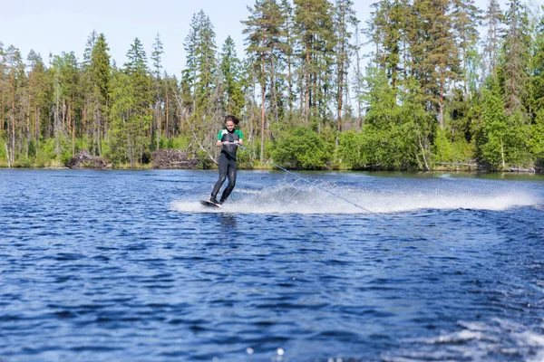 Young pretty slim brunette woman in wetsuit riding wakeboard on wave of motorboot — Stockfoto