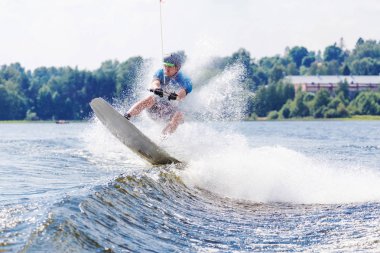 Genç, aktif bir adam, yaz gölünde bir motorlu tekneden gelen dalgada wakeboard kullanıyor.
