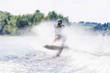 Genç, aktif bir adam, yaz gölünde bir motorlu tekneden gelen dalgada wakeboard kullanıyor.