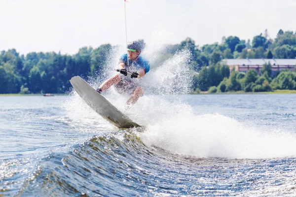 Young active man riding wakeboard on a wave from a motorboat on summer lake — 스톡 사진