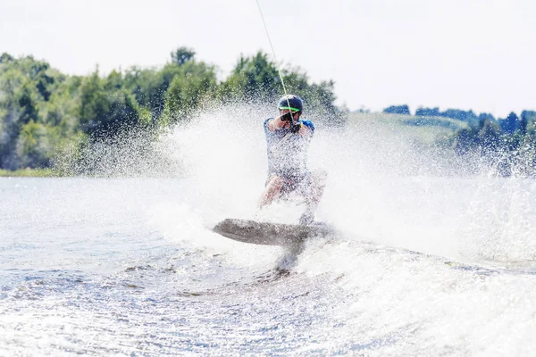 Young active man riding wakeboard on a wave from a motorboat on summer lake — Stock Photo, Image