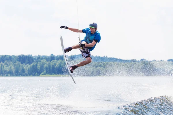 Junger aktiver Mann reitet Wakeboard auf einer Welle von einem Motorboot auf dem Sommersee Stockbild