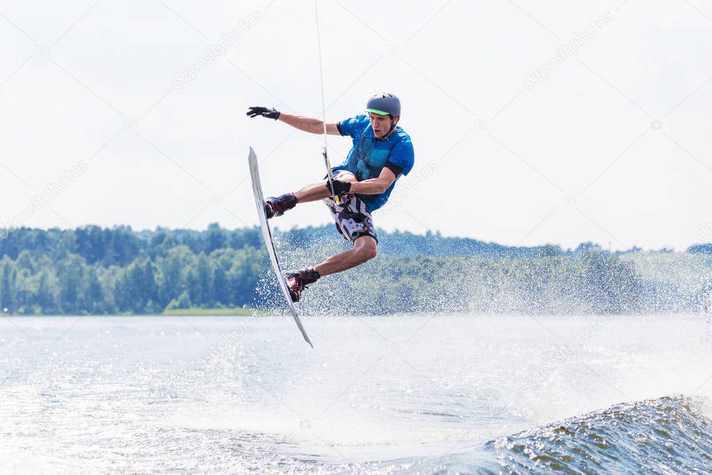 Young active man riding wakeboard on a wave from a motorboat on summer lake