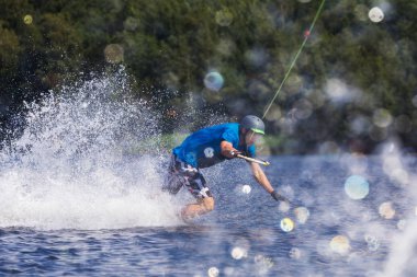 Genç, aktif bir adam, yaz gölünde bir motorlu tekneden gelen dalgada wakeboard kullanıyor.