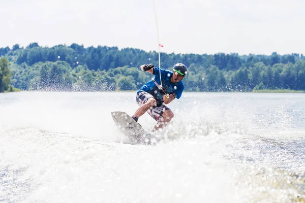 Молодий активний чоловік їде на трампліні на хвилі з моторного човна на літньому озері — стокове фото