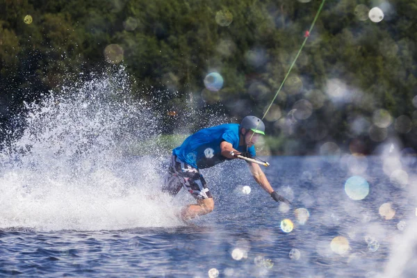 Junger aktiver Mann reitet Wakeboard auf einer Welle von einem Motorboot auf dem Sommersee — Stockfoto