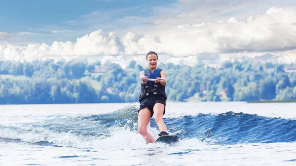 若いですかなりスリムブルネット女性乗馬wakeboard上の波の上にモーターボートで夏の湖 — ストック写真