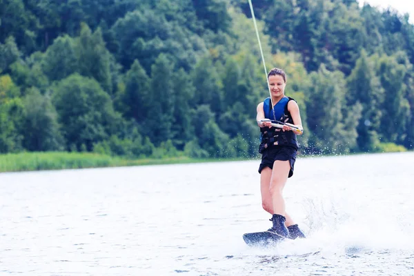 Young pretty slim brunette woman riding wakeboard on wave of motorboat in summer lake Royalty Free Stock Images