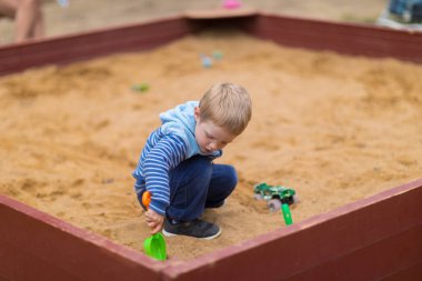 Küçük çocuk çocuk oyun alanında kum havuzunda bir oyuncak araba ile oynuyor