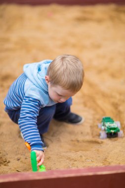 Küçük çocuk çocuk oyun alanında kum havuzunda bir oyuncak araba ile oynuyor