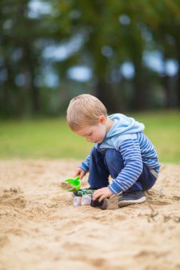 Küçük çocuk çocuk oyun alanında kum havuzunda bir oyuncak araba ile oynuyor