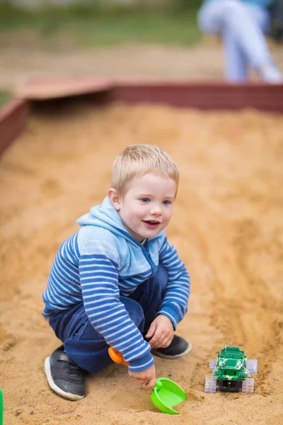 Küçük çocuk çocuk oyun alanında kum havuzunda bir oyuncak araba ile oynuyor
