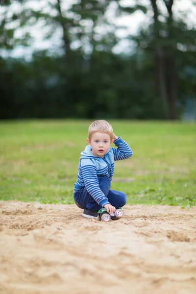 Little boy playing with a toy car in the sandbox on children playground — Stock Photo, Image