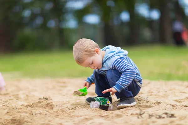 Kleiner Junge spielt mit Spielzeugauto im Sandkasten auf Kinderspielplatz Stockbild