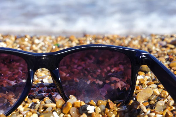 Plastové sluneční brýle na pozadí moře kamenů. Moře v pozadí — Stock fotografie