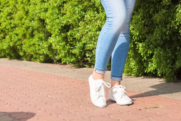 Λευκά αθλητικά παπούτσια σε γυναικεία πόδια σε μπλε τζιν — Φωτογραφία Αρχείου