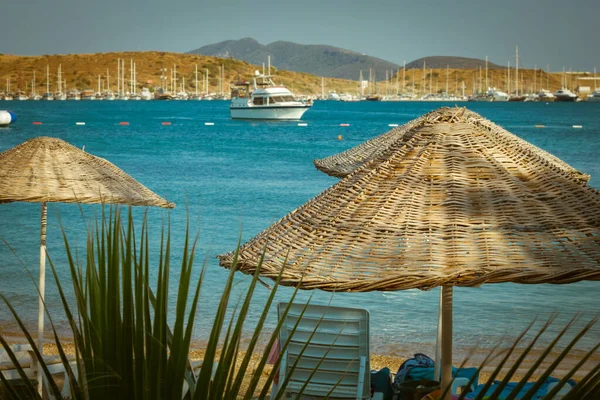 Соломенные зонтики, пляжные зонтики на фоне моря с размытыми яхтами — стоковое фото