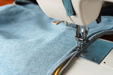 Dikiş makinesi. Mavi kumaştan dekoratif bir kordon dikme işlemi.