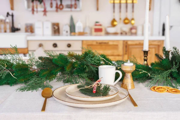 Noel dekoru. Güzel düzenlenmiş yemek masası, zarif beyaz tabaklar, beyaz masa örtüsü üzerinde altın çatal bıçak takımı ve ladin çelengi, aile ve arkadaşlarla yemek için bayram atmosferi yaratıyor..