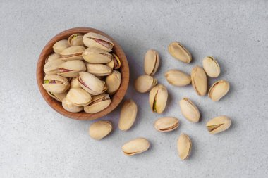 Yaklaş, ahşap kasedeki tuzlu fıstıklı fındık makrosu. Tohumları açık gri arka planda serpiştirilmiş. Sağlıklı abur cubur fotoğrafçılığı, organik fındık, doğal doku, temiz yeme konsepti.