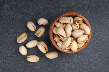 Yaklaş, ahşap kasede tuzlu şam fıstığı fındığı ve koyu gri arka plana serpiştirilmiş tohumlar. Sağlıklı abur cubur fotoğrafçılığı, organik fındık, doğal doku, temiz yeme konsepti.