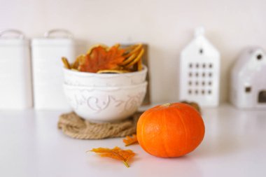 Kurumuş portakal dilimleri, turuncu balkabağı ve arka planda sıcak kithen ile renkli sonbahar yapraklarıyla dolu beyaz kase. Ev sonbaharı dekorasyonu, güzel sofra takımı.