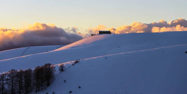 Barn at the top of a hill at twilight in winter, snowy hill in a natural park in Northern italy