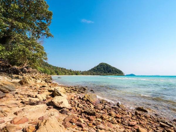 Glimpse of a crystalline sea and a wild vegetation with a hill on the background viewed from a rock on the coast