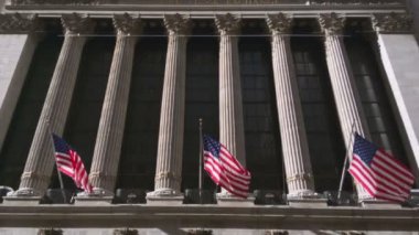 Sütunların tabanına yerleştirilen Amerikan bayraklarından başlayıp köşe yazılarının en tepesindeki Wall Street borsasına kadar uzanan dikey hareket.