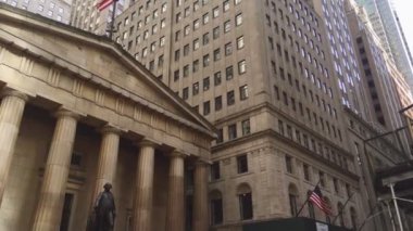 Kameranın dikey hareketi Federal Hall Ulusal Müzesi 'ni gösteriyor. Önünde George Washington' un bronz heykeli, arkasında da gökdelenler var.