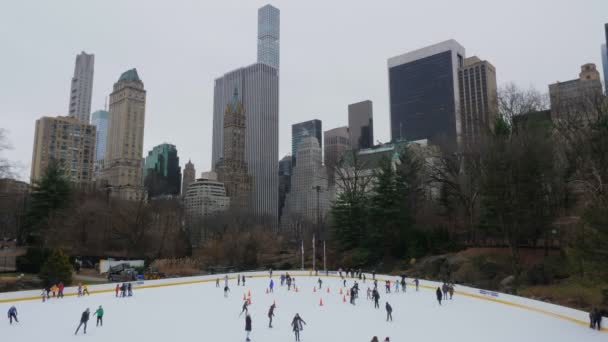 都会の大高層ビルを背景に 灰色と曇りの日に友達と中央公園のスケートリンクを共有することで アイススケートを楽しむ — ストック動画