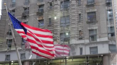 Bir Amerikan bayrağı, bayrağın kendisini ve karşıdaki binanın ön cephesini yansıtan bir binanın aynalı cephesinin önünde hafifçe dalgalanıyor.