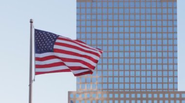 Güneşli bir günde gökdelenlerin aynalı cepheleriyle arka planda mavi gökyüzü dalgalanan Amerikan Yıldızları ve Şeritleri 'nin ön görüntüsü.