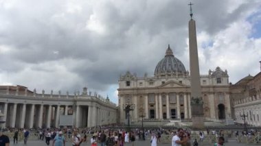 Roma - Eylül 2019 - Roma 'da Piazza San Pietro yazın bulutlu bir günde turistlerle doludur, ön planda bir çift ünlü bazilika ve arkasında dikilitaşıyla selfie çeker.