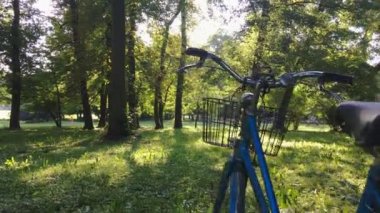 Güneşli, huzurlu bir yaz günü, parkta, ağaçların altında, mavi bir bisikletle. Dolly ileri sardı