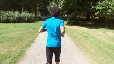 Mavi tişörtlü genç sporcu Monza kraliyet villasının parkının yolunda koşuyor. Kamera onu takip ediyor.