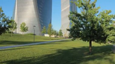 Milano 'nun Citylife semtindeki şehir parkındaki modern camlı gökdelenlere doğru çimlerin üzerinde yürüyen bir insanın bakış açısı. Bazı insanlar çimlerin üzerinde güneşli günün tadını çıkarırlar.